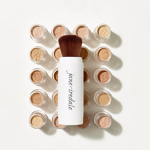 Set of jane iredale makeup products including a brush and small containers with beige powders on a light background.